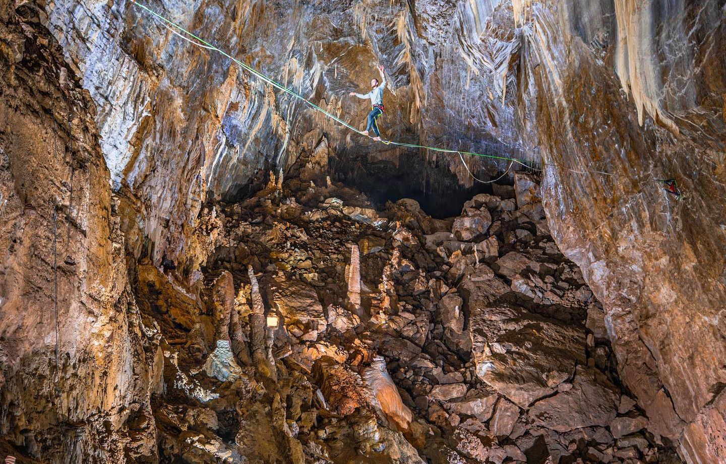 Un slackliner traverse une grande salle souterraine aux parois couvertes de concrétions
